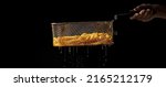 Crop unrecognizable chef holding metal deep fryer basket with French fries and dripping oil against black background