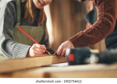 Crop unrecognizable craftswoman making marks on wooden detail while working with anonymous colleague in carpentry workshop