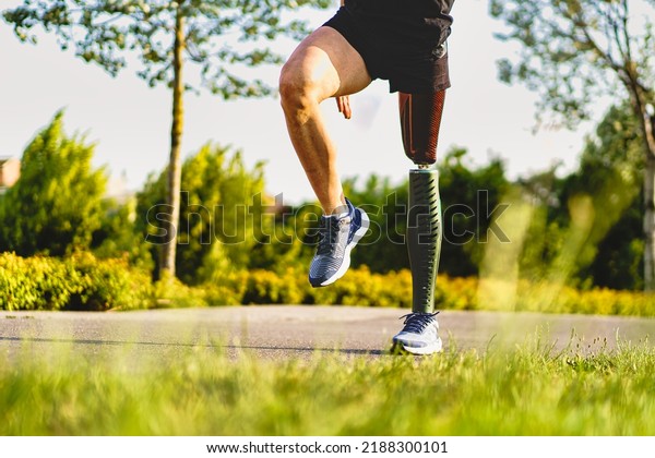 Crop view of disabled athlete man with prosthetic\
leg exercising outdoors in the parkland - health and people\
lifestyle concept