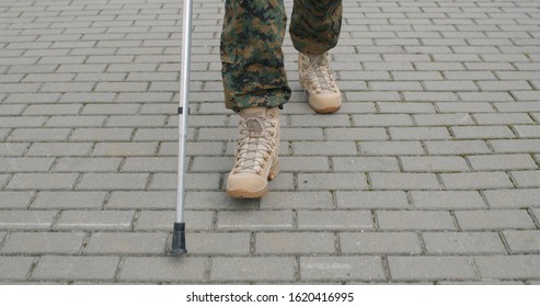 Crop View Of Injured Soldiers Boots Walking With Crutch. Front View. Returning Home After Military Deployment Concept Of Military Servise, Army, Trauma