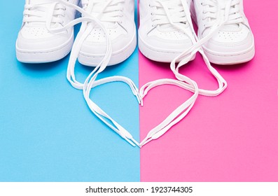 Crop View Of Matching White Sneakers And A Heart Symbol Made Of The Shoelaces On A Pink Blue Background. Romantic Concept For Couples Wearing Matching Outfits.