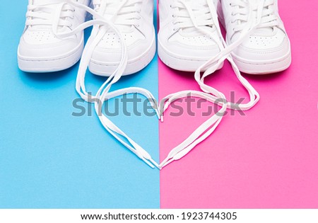 Crop view of matching white sneakers and a heart symbol made of the shoelaces on a pink blue background. Romantic concept for couples wearing matching outfits.
