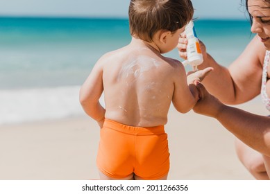 Crop Woman Applying Sunblock Cream From Bottle To Hand Of Shirtless Toddler Baby While Spending Sunny Summer Day On Beach