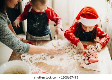 Crop woman helping adorable kids in making Christmas cookies at messy table in floor using cutters