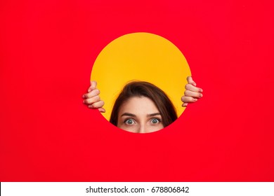 Crop woman looking out of circle cut in red paper on yellow background. 