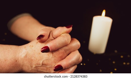Crop woman praying with clasped hands. Crop unrecognizable religious female praying with folded hands at dark table with burning candle.