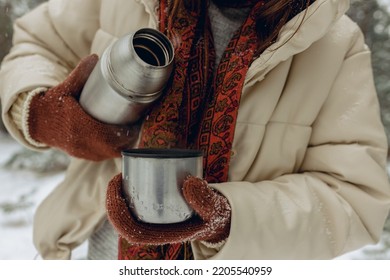 Crop Woman In Warm Outerwear Pouring Hot Tea Or Coffee From Metal Thermos In Cup In Snowy Forest In Winter 