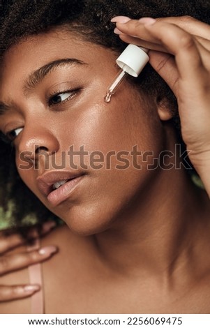 Crop young female applying serum on face. Closeup of black young woman using facial cosmetic product. Beauty and skincare concept