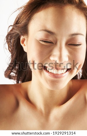 Crop young happy Asian female with perfect skin and dimples smiling with closed eyes against white background