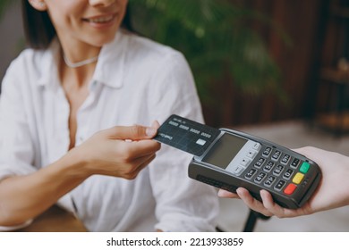 Croped young smiling fun happy woman wearing white shirt hold wireless bank payment terminal to process acquire credit card sit alone at table in coffee shop cafe restaurant indoor. Focus on machine
