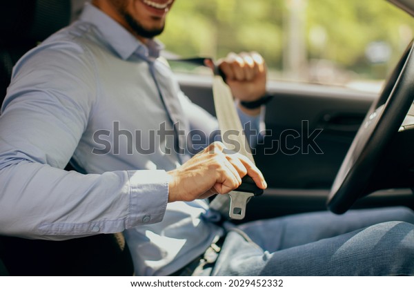 Cropped of arab guy in formal outfit fastening\
automobile seatbelt, closeup of middle-eastern man entrepreneur\
driving nice car, going to office, sde view, copy space. Safety\
driving concept