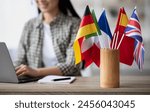 Cropped of asian young woman foreign language teacher sitting at workdesk and using laptop, selective focus on international flags. Foreign language online course, class, e-education concept
