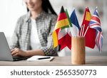 Cropped of asian young woman foreign language teacher sitting at workdesk and using laptop, selective focus on international flags. Foreign language online course, class, e-education concept