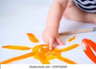 Cropped Baby Crawls On The Floor Playing With Paint, Showing Finger Yellow Painted Sun Close Up. Happy Leasure And Play At Home. Summer.