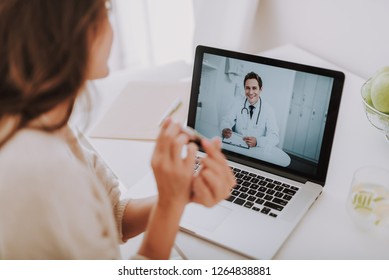 Cropped back rear view of expectant mother sitting in light living room and using pc laptop while talking with smart doctor. She showing pregnancy test in camera