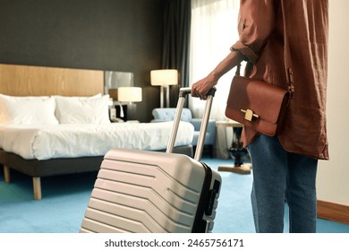 Cropped back view of African American woman entering hotel room and holding suitcase copy space