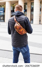 A Cropped Beyond Recognition Man Holding His New Brown Leather Banana Bag In The City. Men's Leather Hip Bag Over The Shoulder Waist Bag Made Of Genuine Leather. The Man Is Standing With His Back