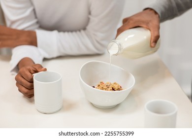 Cropped of black couple in pajamas have breakfast together at home. Unrecognizable african woman holding mug with tea or coffee, man pouring milk into granola bowl. Diet, nutrition concept - Powered by Shutterstock