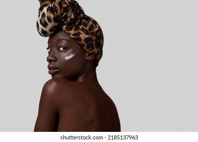 Cropped Of Black Girl With Cosmetic Cream On Face Looking At Camera. Pretty Young Slim Woman Wear Traditional African Turban. Body And Skin Care. Isolated On White Background. Studio Shoot. Copy