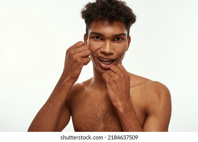 Cropped Of Black Guy Brushing His Teeth With Dental Floss. Young Brunette Curly Man With Naked Torso Looking At Camera. Dental Care And Hygiene. Isolated On White Background. Studio Shoot. Copy