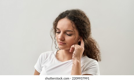 Cropped Of Caucasian Teenage Girl With Closed Eyes Push On Wireless Earphone For Choose Music. Curly Female Of Zoomer Generation. Modern Youngster Lifestyle. White Background. Studio Shoot. Copy Space