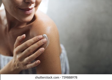 Cropped Caucasian woman putting body lotion on her shoulder.