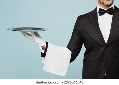 Cropped close up adult barista male waiter butler man wear shirt black suit bow tie uniform hold in hand metal tray plate work at cafe isolated on plain blue background. Restaurant employee concept - Powered by Shutterstock