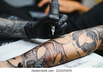 Cropped close up of a bearded tattoo artist working at his studio tattooing sleeve on the arm of his male client. Man getting tattooed by professional tattooist - Shutterstock ID 2125291070