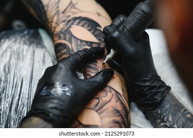 Cropped close up of a bearded tattoo artist working at his studio tattooing sleeve on the arm of his male client. Man getting tattooed by professional tattooist