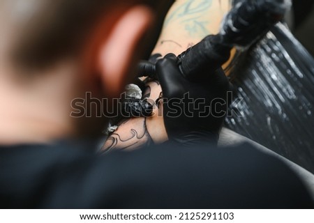 Cropped close up of a bearded tattoo artist working at his studio tattooing sleeve on the arm of his male client. Man getting tattooed by professional tattooist