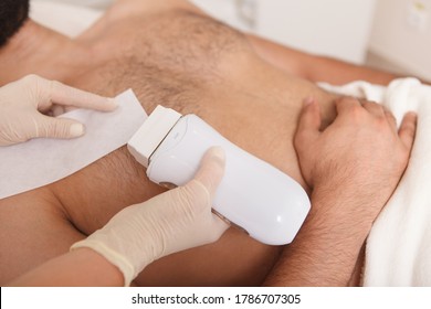 Cropped close up of beautician using hot wax and paper strips, removing chest hair of male client