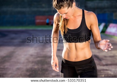 cropped close up body of fit young woman in start position in stadium in summer. She is wearing shorts and sport top showing slim beautiful stomach and abs