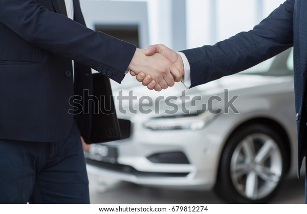 Cropped close up of car dealer shaking hands with\
his male customer selling buying cars sales seller offer agreement\
deal partnership men contract business meeting success people\
greeting concept