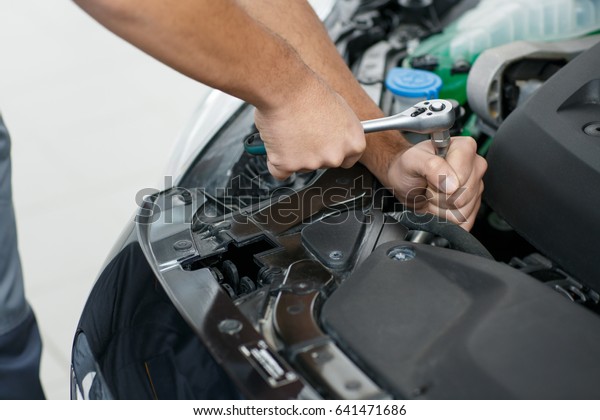 Cropped close up of a car repairman using wrench
while repairing a car at his garage profession professionalism
tools instruments equipment industry automotive vehicle transport
fixing concept