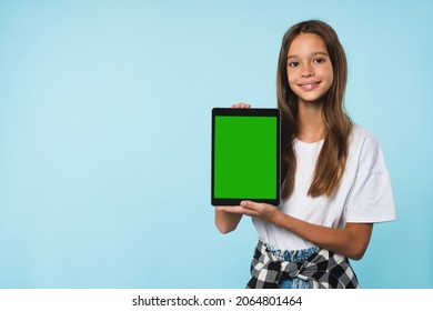 Cropped close up cutout portrait of smiling caucasian schoolgirl teenager child pupil student holding digital tablet showing blank screen with advert place mockup isolated in blue background