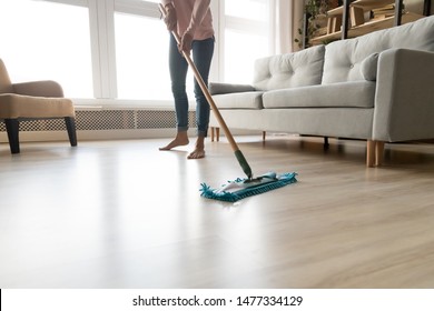 Cropped close up image of barefoot young woman in casual clothes washing heated wooden laminate warm floor using microfiber wet mop pad, doing homework cleaning routine, housekeeping job concept