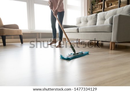 Cropped close up image of barefoot young woman in casual clothes washing heated wooden laminate warm floor using microfiber wet mop pad, doing homework cleaning routine, housekeeping job concept Imagine de stoc © 