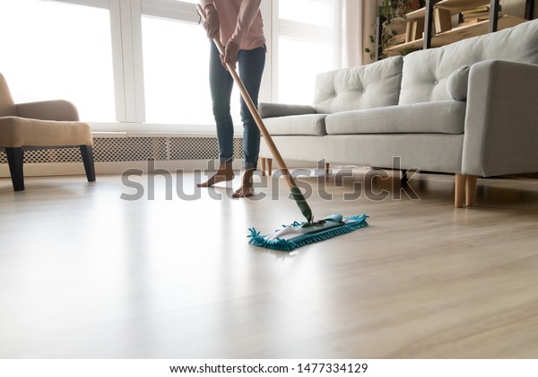 Cropped close up image of barefoot young woman in\
casual clothes washing heated wooden laminate warm floor using\
microfiber wet mop pad, doing homework cleaning routine,\
housekeeping job\
concept