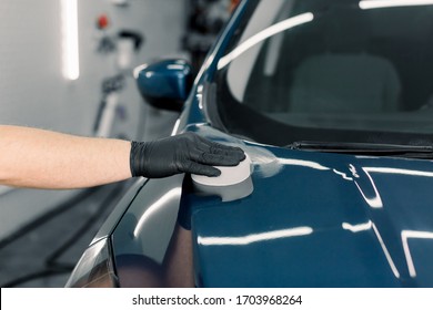 Cropped Close Up Image Of Male Hand In Protective Black Glove, Holding White Sponge With Solid Carnauba Wax, And Polishing Hood Of Luxury Blue Car At Professional Detailing Workshop. Car Detailing