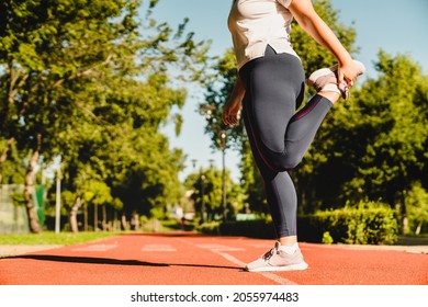 Cropped close up image of sporty young plump plus-size body positive woman athlete stretching her leg before yoga class training losing weight in fitness outfit in stadium