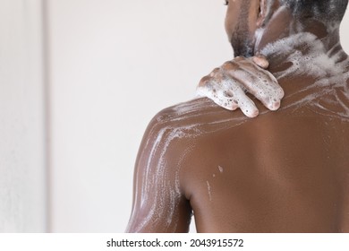 Cropped close up male body part, back and shoulder of African man take shower wash body use soap, hydrating gel, do morning self-hygiene routine. Skincare, bodycare product for men, healthcare concept