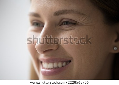Cropped close up part of female face, happy young Caucasian woman portrait look aside, having white-toothed smile, wrinkles around eyes, staring into distance. Natural beauty, skincare treatments ad
