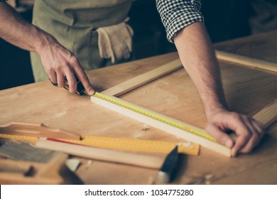 Cropped close up photo of cabinet-maker's strong hands, the master is measuring a wooden frame using roulette on the work-table