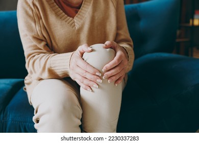 Cropped close up photo of pensioner woman wear casual clothes sits on blue sofa hold knee suffer from leg knee pain inflammation stay home flat spend free spare time in living room indoor grey wall - Powered by Shutterstock