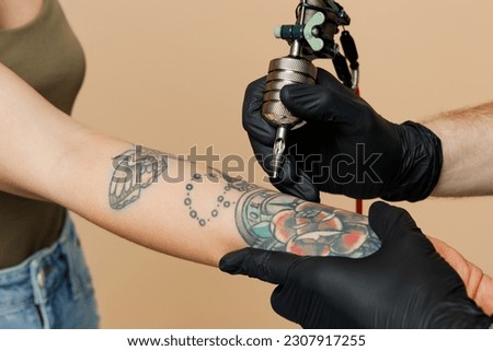 Cropped close up photo of tattooer master artist tattooed man wears black sterile gloves hold machine black ink in jar, equipment for making tattoo art on body hand isolated on plain beige background