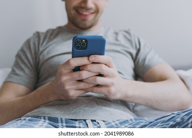 Cropped Close Up Photo Young Man In Pajamas Grey T-shirt Lying Sit In Bed Read Message Mobile Cell Phone Chat Online Rest Relax At Home Indoors Bedroom Good Mood Sleeping Night Morning Bedtime Concept