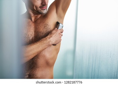 Cropped close up portrait of handsome gentleman with wet body using electric razor to remove hair from underarm. Copy space in right side