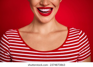 Cropped close portrait of young lovely lady showing perfect smile licking teeth wearing striped t shirt isolated on red color background