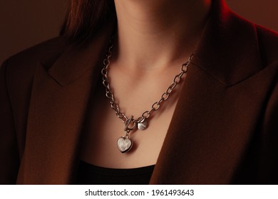 Cropped close up portrait of young woman with perfect silky skin, demonstrating silver jewelry chain with medallion on the neck in a brown jacket - Shutterstock ID 1961493643