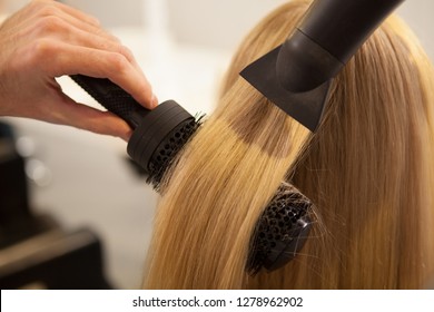 Cropped close up of a professional hairdresser using round brush and blow dryer, styling long blond hair of his female client. Healthy strong hair of a woman during new hairstyle treatment, copy space - Powered by Shutterstock